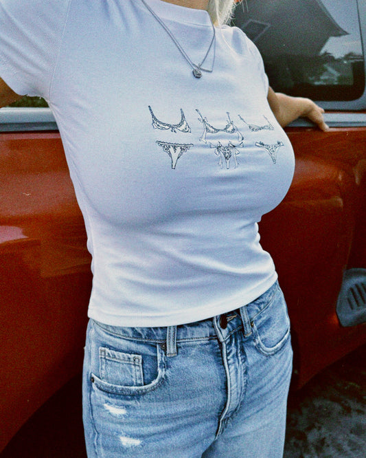 Person wearing a white t-shirt with graphic design in front of a red vehicle.